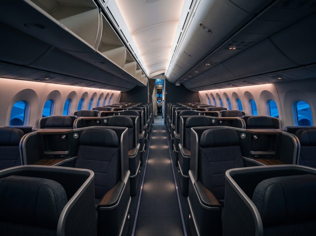 Wide view down the aisle of an empty business-class cabin at night, sculpted seat shells receding in alternating rows under blue-hour light.