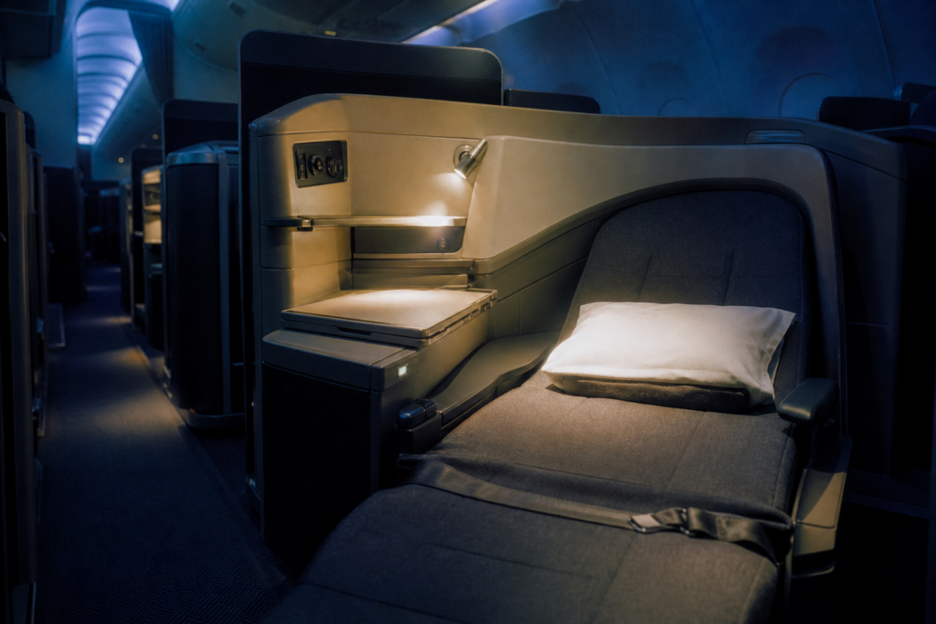 Premium aircraft business class cabin interior with flat-bed seats and privacy dividers, photographed from the aisle with indirect lighting