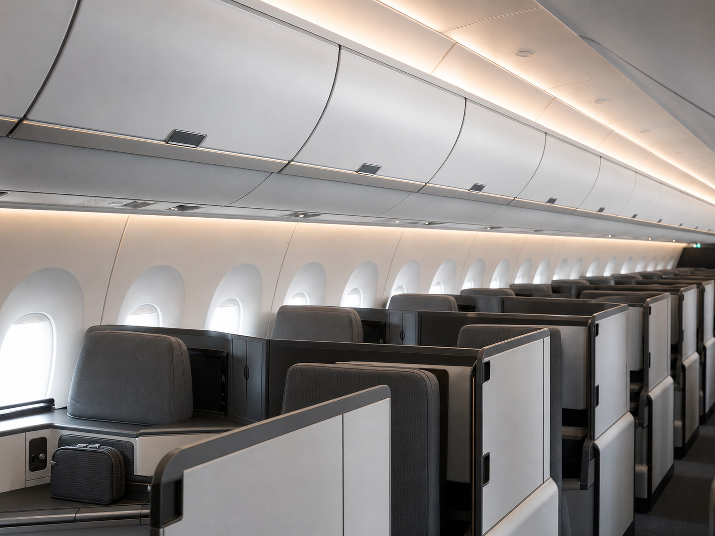 The overhead bin line of a wide-body long-haul cabin seen from the aisle, with one cabin bag stowed on a seat below